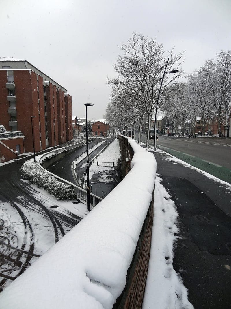 Allées Charles-de-Fitte : allées bordées d’arbres enneigés, mur couvert de neige, immeuble de brique rouge à gauche