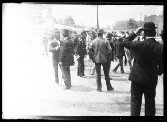 Photographie ancienne : foule d'hommes en chapeau, vus surtout de dos, sur une place
