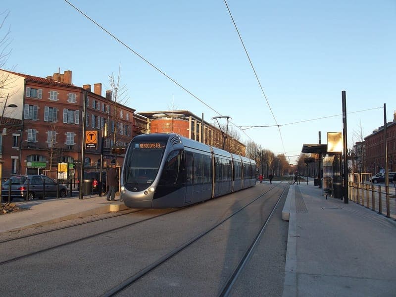 Avenue Maurice-Hauriou : tramway à l’arrêt le long d’immeubles de brique, sous un ciel dégagé, avec arbres et arrêt couvert