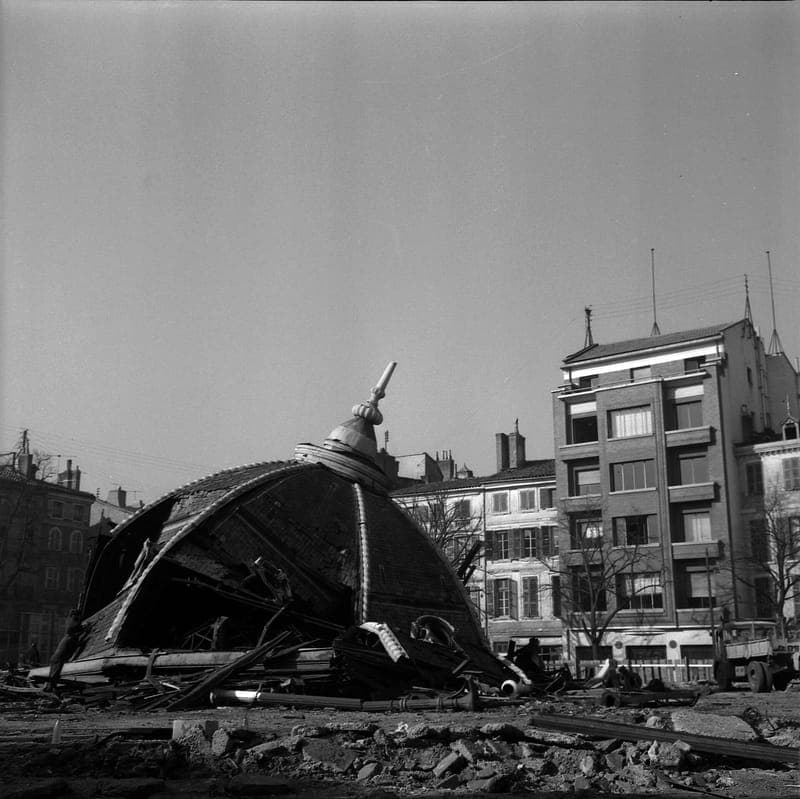 Coupole de la halle écrasée au sol parmi les gravats, immeubles en arrière-plan, photographie en noir et blanc