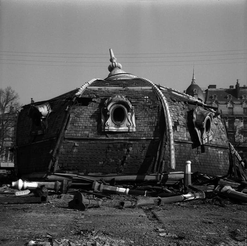 Gros plan de la coupole de la halle posée au sol, lucarnes rondes, gravats, noir et blanc