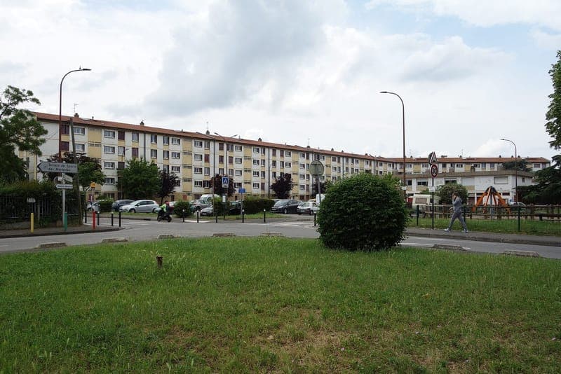 Longue barre d’immeubles derrière une pelouse, rond-point et un passant
