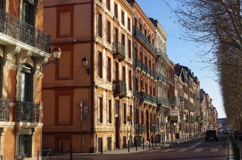 Quai de Tounis : rue bordée de hauts immeubles de brique aux balcons de fer forgé, platanes nus, ciel bleu