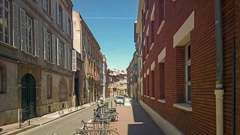 Rue de la Dalbade : rue étroite en perspective, façades de brique de chaque côté, vélos garés, ciel bleu