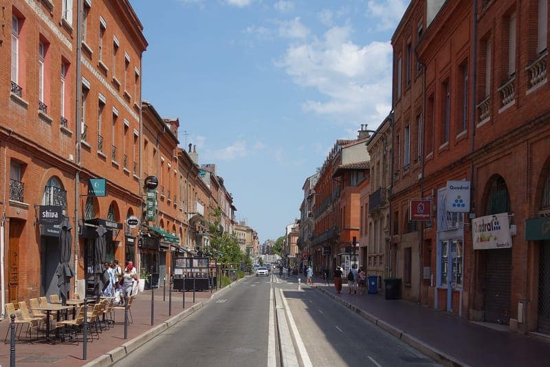 Rue de la République : longue rue bordée de façades de brique, terrasses de café, ciel bleu, circulation au loin