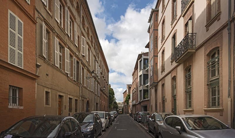 Rue des Renforts : rue étroite bordée d'immeubles de brique, voitures garées des deux côtés