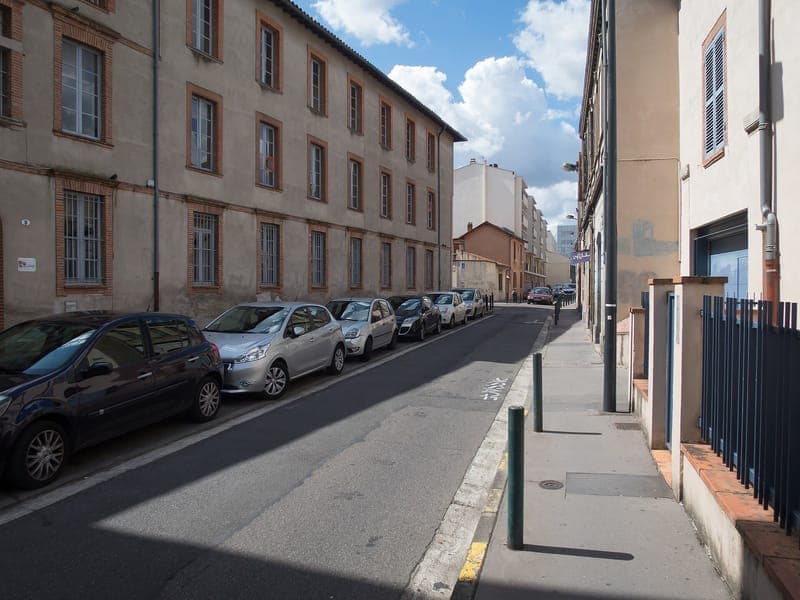 Rue des Teinturiers : rue en ombre et lumière, voitures garées à gauche, façades de brique et trottoir étroit à droite