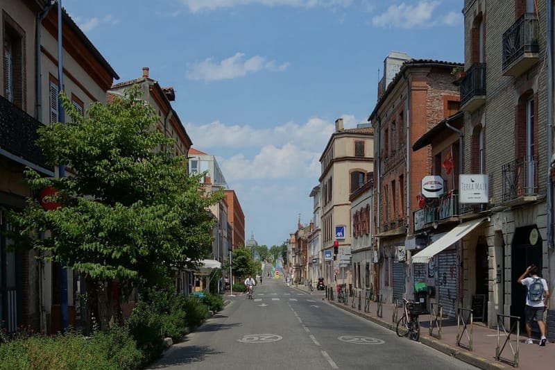 Rue du Pont-Saint-Pierre : rue en perspective bordée d’immeubles de brique, cycliste au loin, dôme au fond et ciel bleu