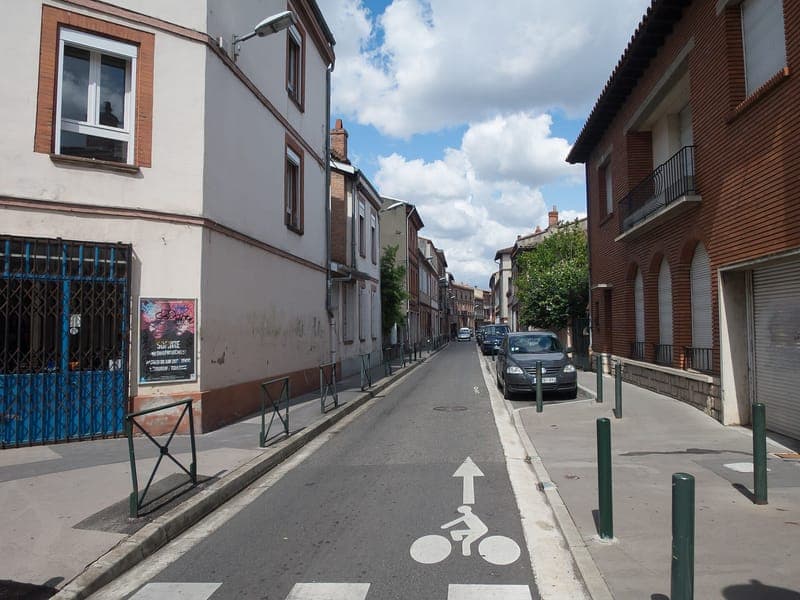 Rue Joseph-Vié : rue étroite avec bande cyclable, façades crépies et immeubles de brique, ciel nuageux