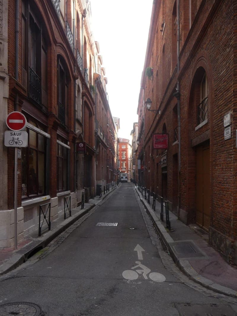 Rue Joutx-Aigues : rue très étroite entre deux hauts murs de brique, piste cyclable peinte au sol