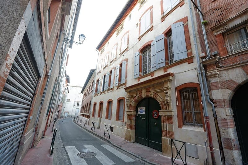 Rue Saint-Rémésy : rue étroite en perspective, façade claire à volets bleus et porte verte à encadrement de brique