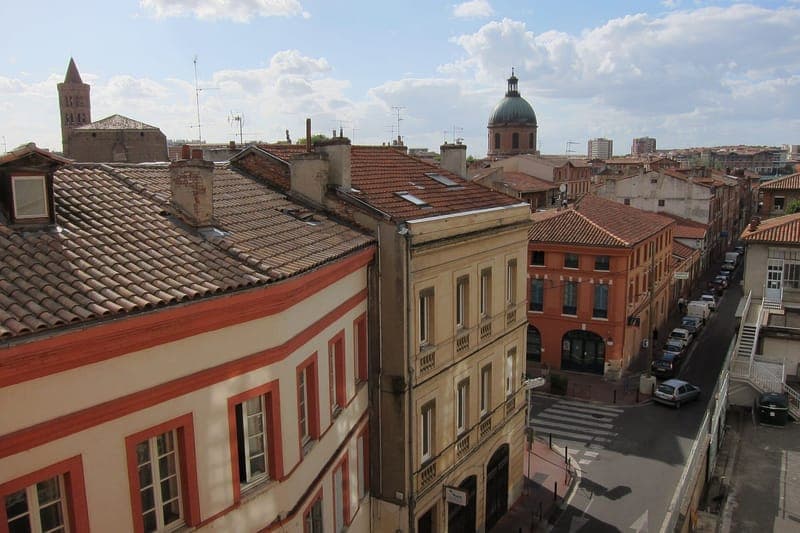 Rue Viguerie : toits de tuiles et façades de brique, rue en contrebas, dôme et clocher au loin