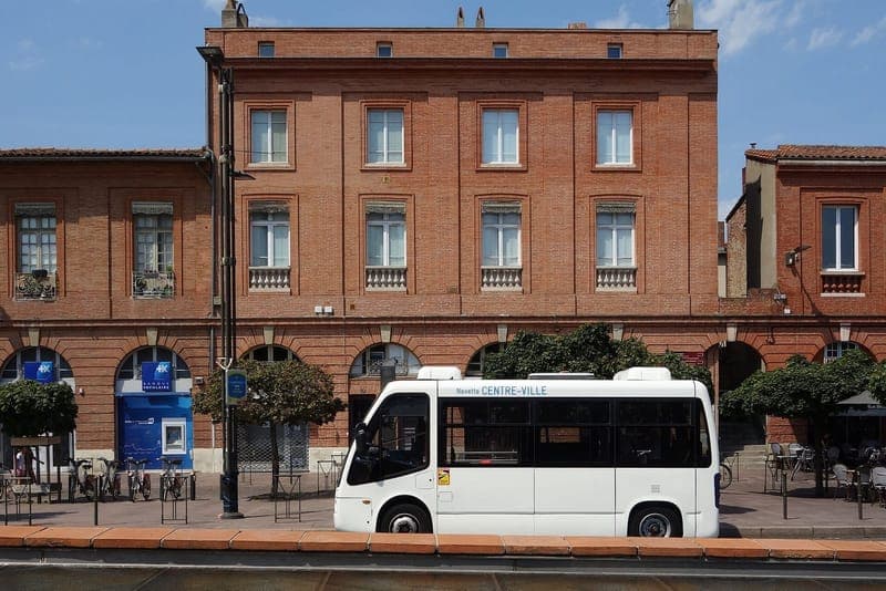 Façade de brique à arcades sur la place Saint-Cyprien, navette blanche devant