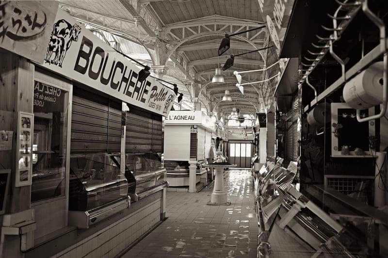 Allée vide du marché couvert en noir et blanc, étals fermés sous une charpente métallique