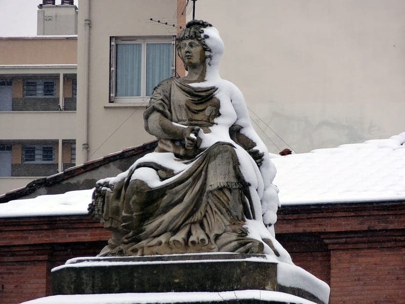 Statue de pierre assise recouverte de neige devant un toit de tuiles