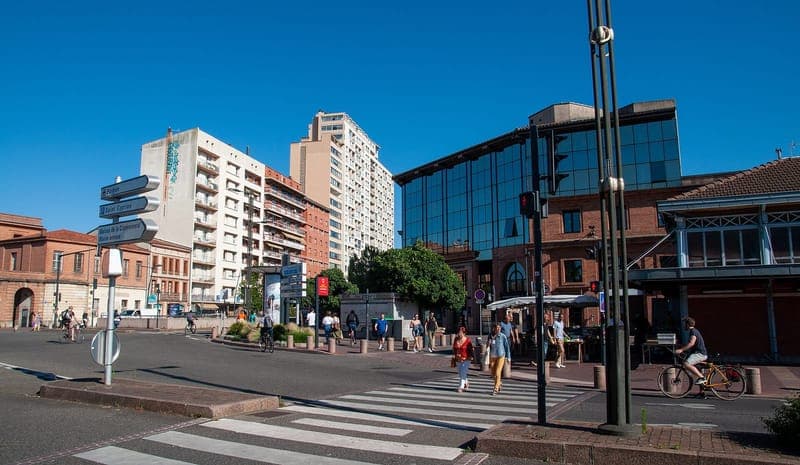Carrefour ensoleillé, immeubles de brique et tours, passants et cycliste